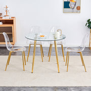 A modern minimalist style round transparent tempered glass table with gold metal legs,paired with 4 modern style transparent dining chairs for a luxurious experience.